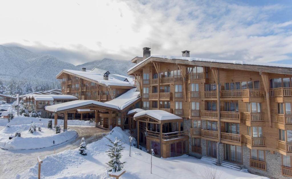 un grand bâtiment en bois avec de la neige au sol dans l'établissement Pirin Golf Hotel & Spa, à Bansko