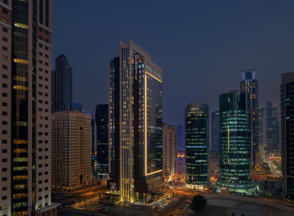 a city skyline with tall buildings at night at Dusit Doha Hotel in Doha