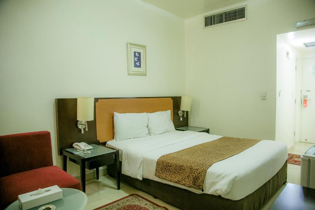 um quarto de hotel com uma cama e uma cadeira vermelha em Phoenicia Grand Hotel em Dubai