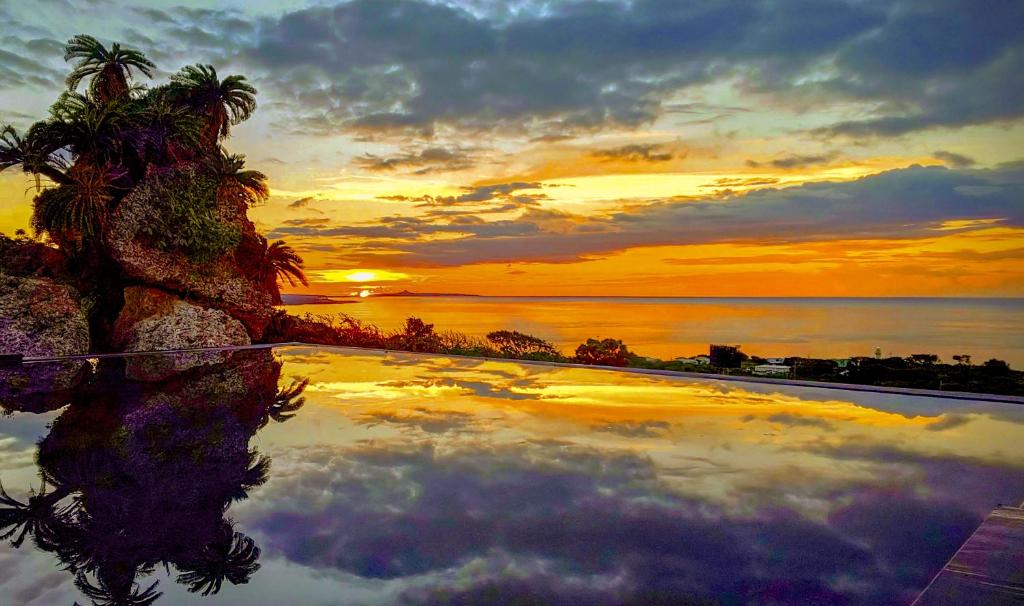 a pool with a palm tree and the sunset at Hanalee Villa Kouri in Nakijin