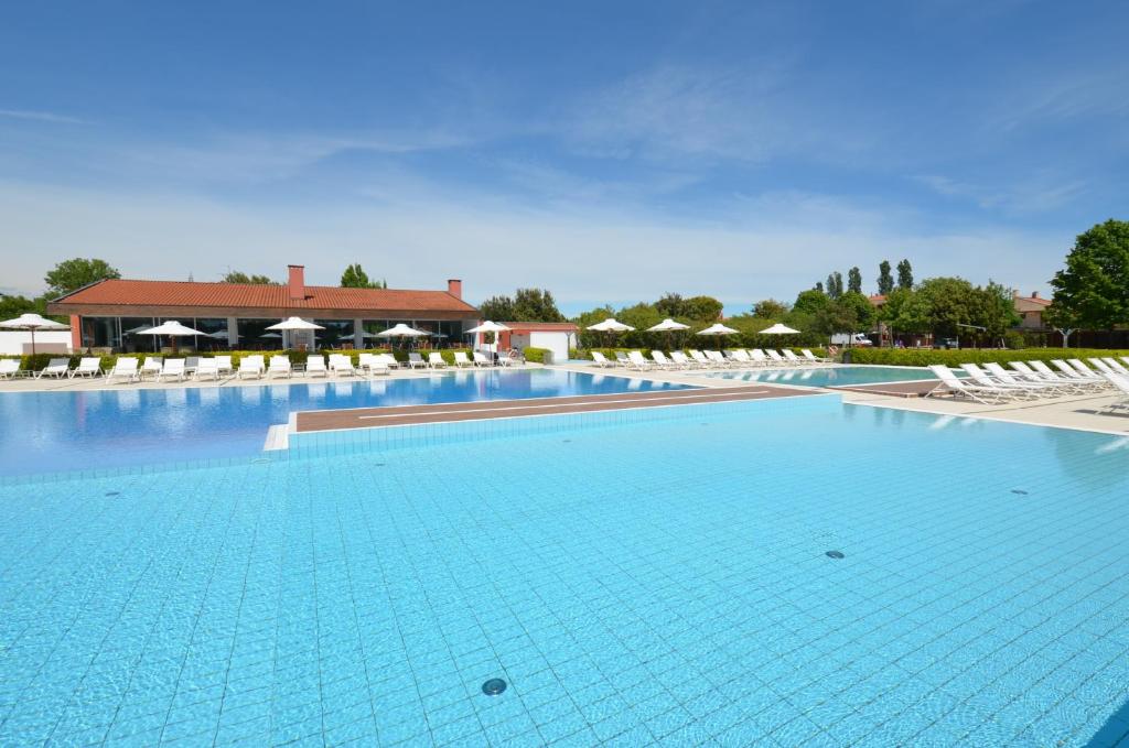 una grande piscina con sedie bianche e un edificio di Magica immobiliare - Golf Jesolo Village 216 a Lido di Jesolo