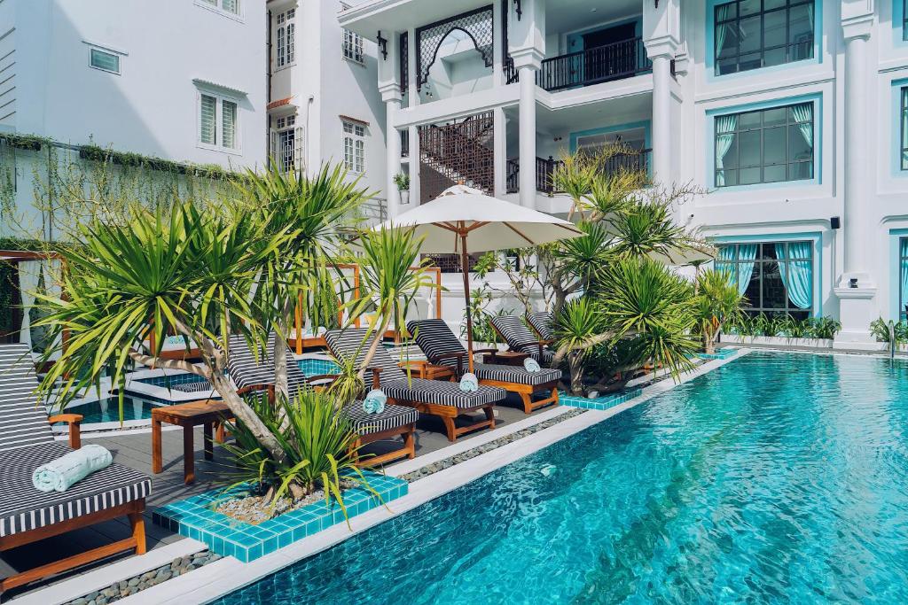 a swimming pool with chairs and an umbrella next to a building at Anio Boutique Hotel Hoian in Hoi An