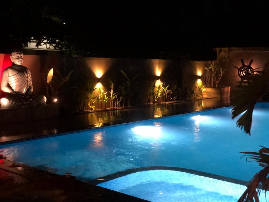 a man sitting next to a swimming pool at night at Haven Alleppey Beach Resort in Alleppey
