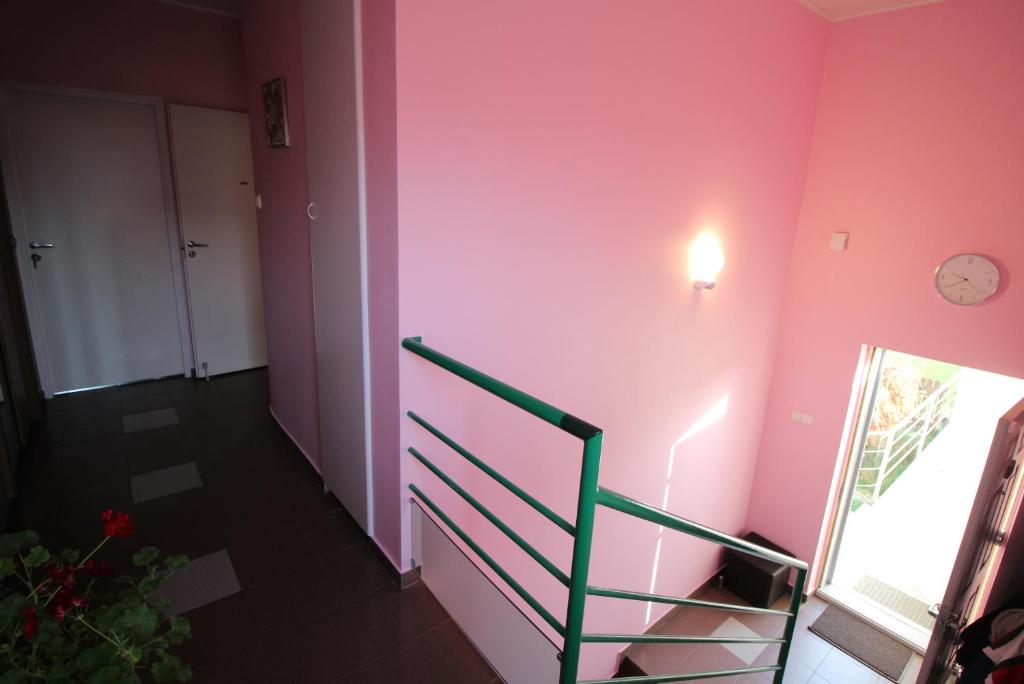 a room with a pink wall with a staircase and a clock at Dangus in Ramučiai