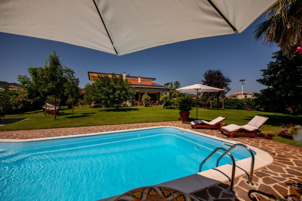 een zwembad met een parasol naast een huis bij Villa Tigli Luxury B&B in Martinsicuro