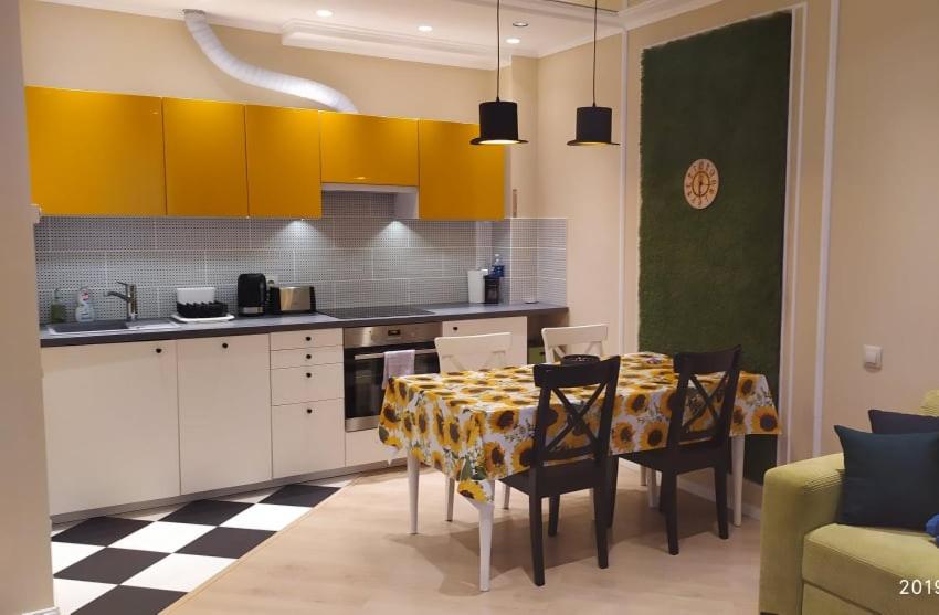 a kitchen with a table with chairs and yellow cabinets at Full House Apartments in Druskininkai