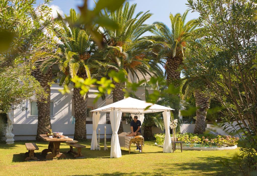 a man sitting under a white tent in a yard with palm trees at Mandraki Village Boutique Hotel in Koukounaries