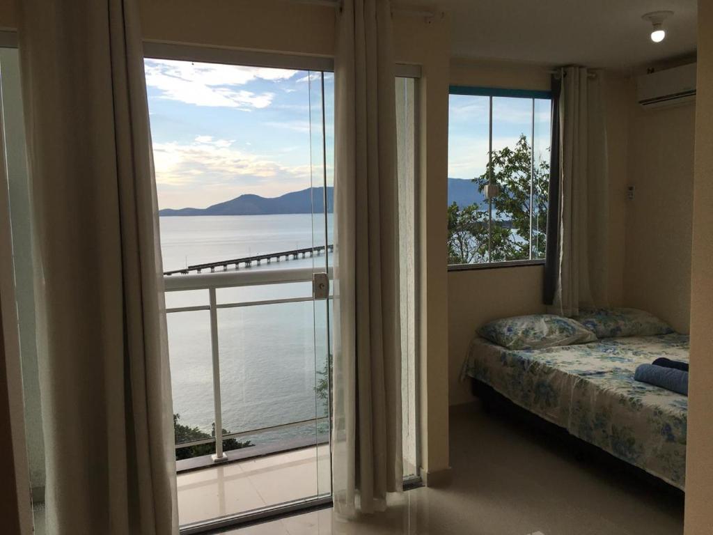 a bedroom with a large window with a view of the water at Pousada Alto de Junqueira in Mangaratiba