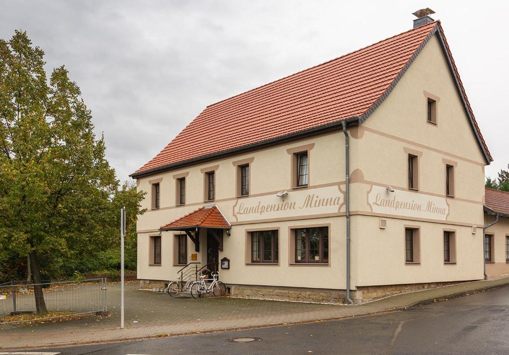a white building with a red roof on a street at Landpension Minna in Herbsleben
