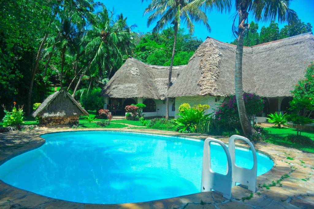 a resort with a large swimming pool with a thatch roof at Fast Care Villa Bavaria in Mombasa