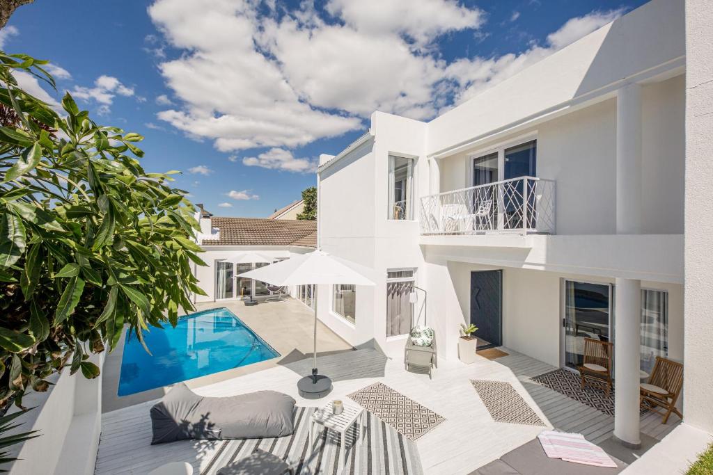 a white house with a swimming pool and a patio at The Little Palm in Bloubergstrand