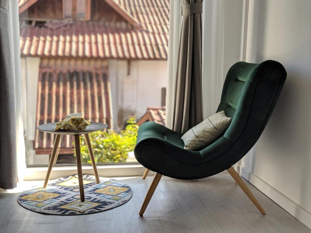 a green chair next to a table and a window at SYRI Boutique Guesthouse Restaurant & Cafe in Vientiane