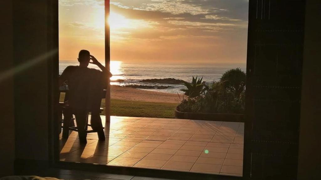 a man sitting at a table watching the sunset at C-Side Apartment Hibberdene in Hibberdene