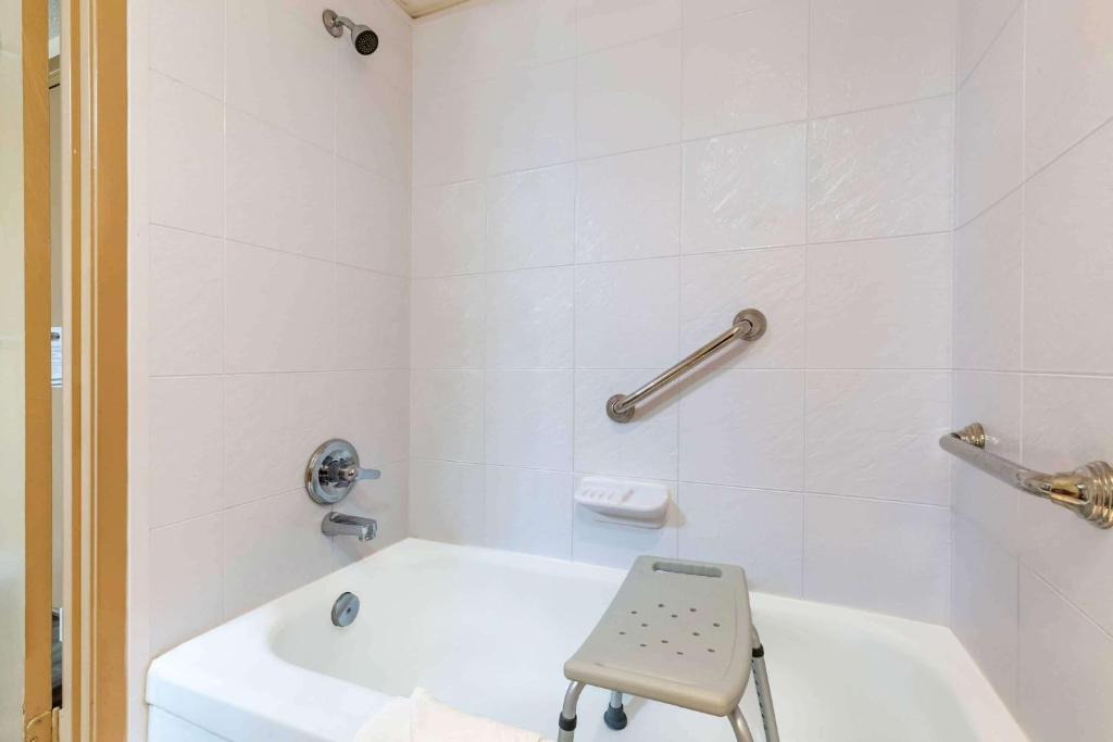 a white bathroom with a white tub and a chair at Ramada by Wyndham Coquitlam in Coquitlam