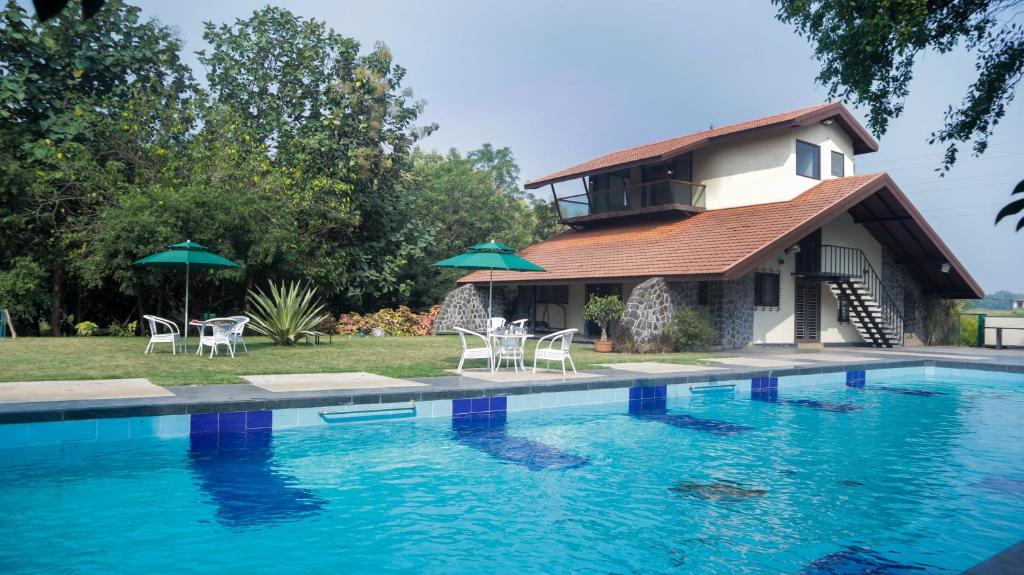 una casa con piscina con sillas y sombrillas en Jungle Safari Resort & Holiday Villa, en Nashik