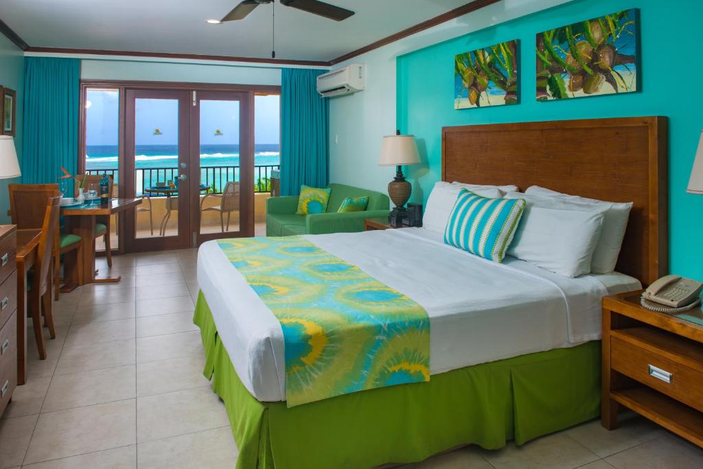 a bedroom with a bed and a balcony with the ocean at Yellow Bird Hotel in Christ Church