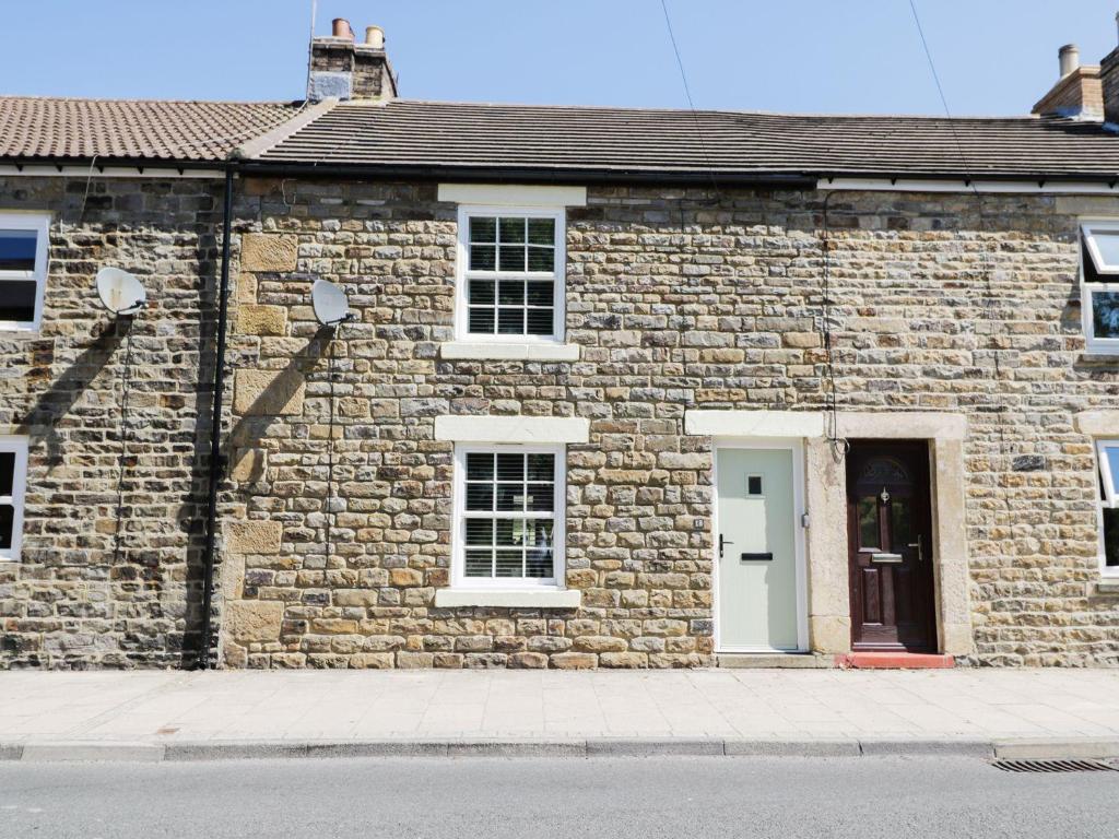 a brick building with a white door on a street at Weardale Cottage in Saint Johns Chapel