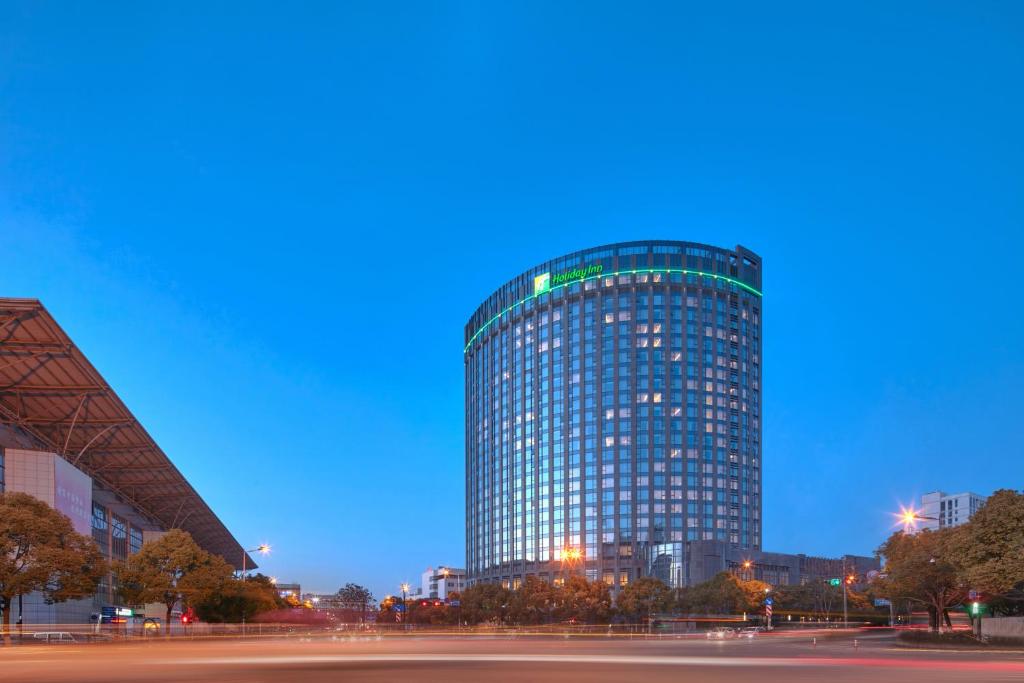 Holiday Inn Express Hangzhou Gongshu, an IHG Hotel في هانغتشو: مبنى زجاجي طويل في الليل في مدينة