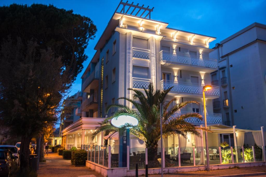 een verlicht gebouw met een palmboom ervoor bij Hotel Vela D'Oro in Riccione