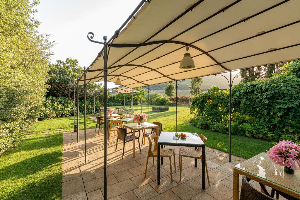 a patio with tables and chairs under an umbrella at Wine Resort Ledà d'Ittiri in Fertilia