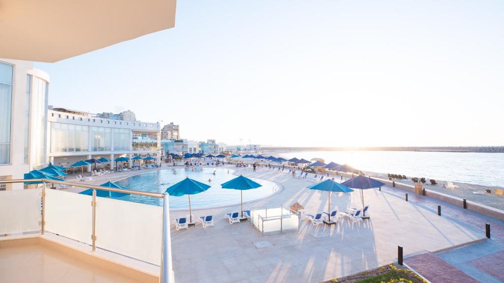 a swimming pool with umbrellas and chairs and the ocean at Golden Jewel Hotel in Alexandria