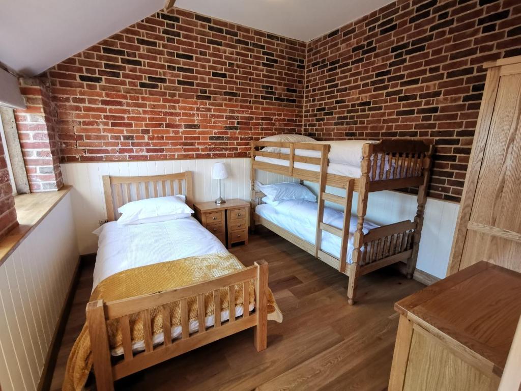 a bedroom with two bunk beds and a brick wall at Blashford Manor Farmhouse Holiday Cottage - The Shire Cottage in Ellingham