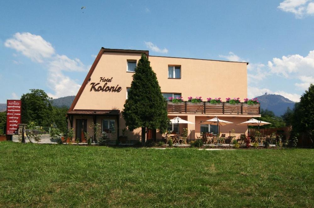 un edificio con tavoli e ombrelloni in un campo di Hotel Kolonie a Frýdlant nad Ostravicí