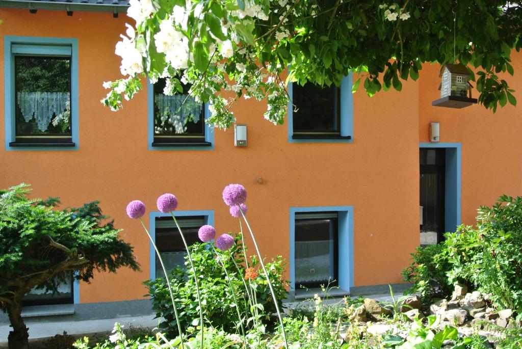 een oranje gebouw met zwarte ramen en paarse bloemen bij Ferienwohnung zur Mühle in Sotzweiler