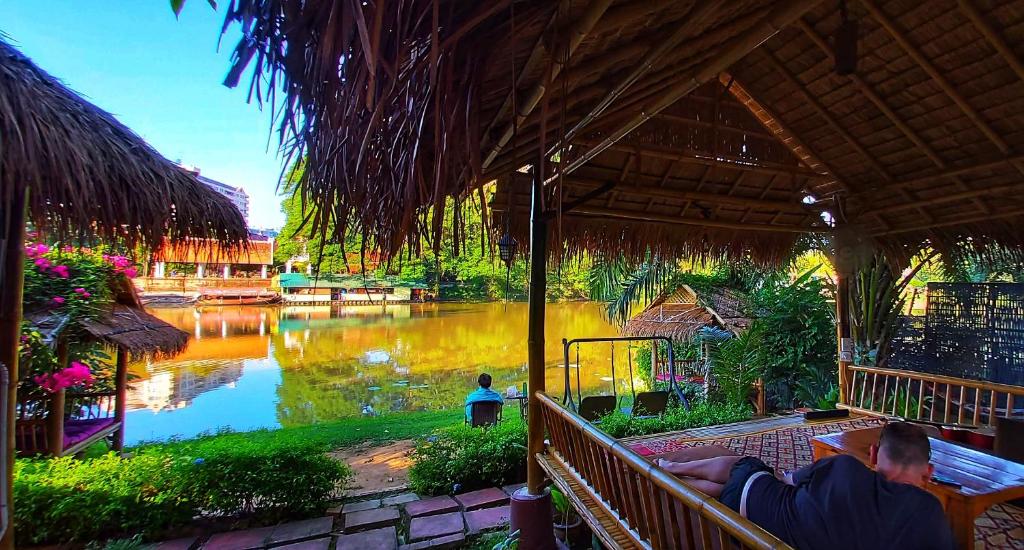 Un uomo seduto su una panchina di fronte a un fiume di Mapping Hostel a Chiang Mai
