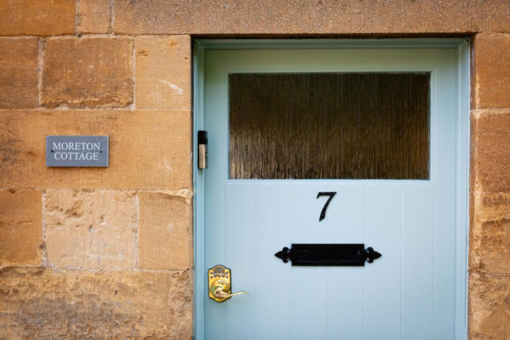 a blue door with a clock on it next to a brick wall at Moreton Cottage in Moreton in Marsh