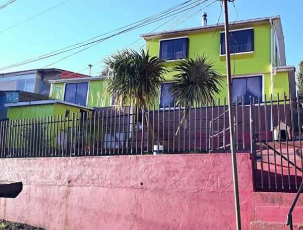 a yellow house with palm trees behind a fence at La Casa del Viento in Talcahuano