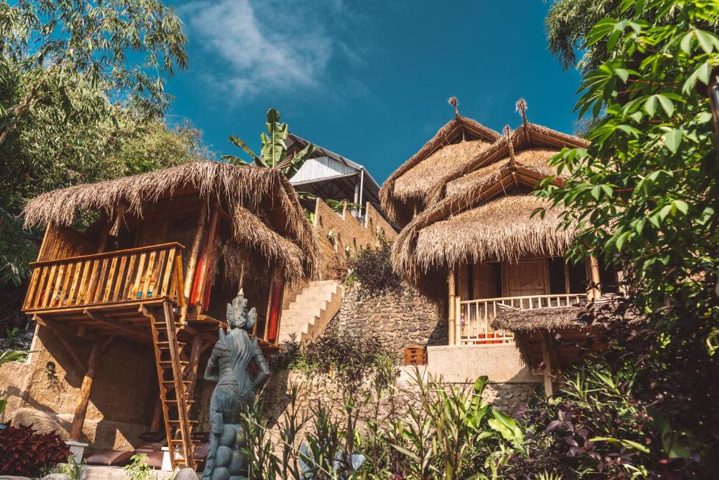 a house with thatched roofs and a statue in front of it at BALI BAMBOO JUNGLE HUTS AND HOSTEL in Tampaksiring