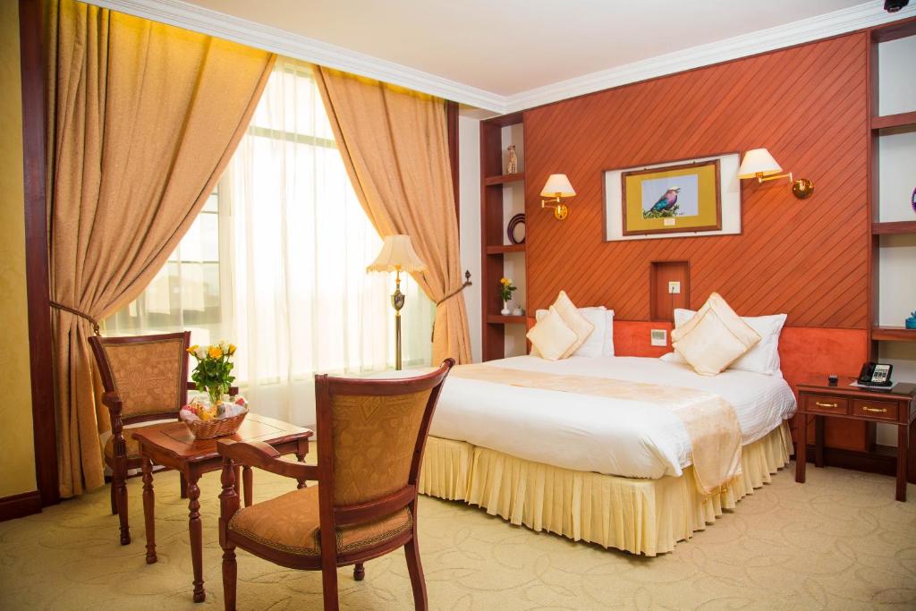 アルーシャにあるPalace Hotel Arushaのベッド、テーブル、椅子が備わるホテルルームです。