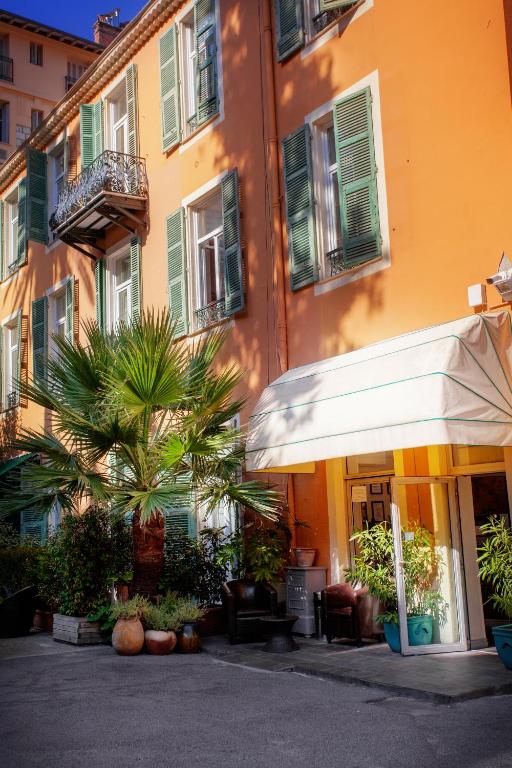 an orange building with a white umbrella and a palm tree at Hôtel restaurant Oasis in Nice