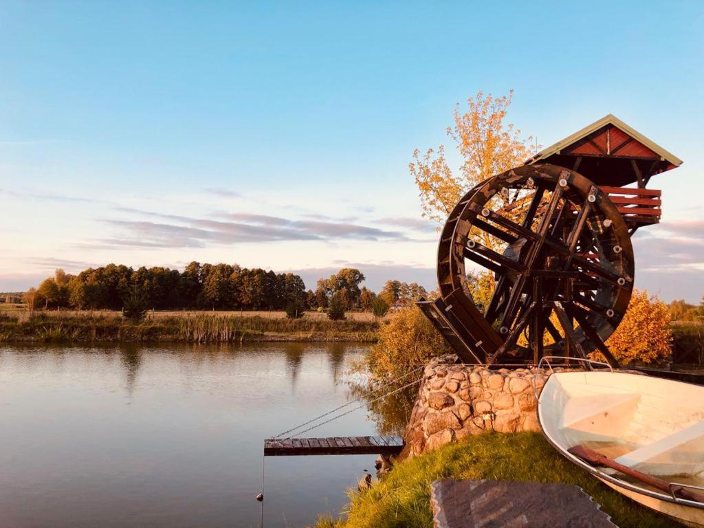 a sculpture of a water wheel next to a river at Dom nad stawem przy lesie in Burkat