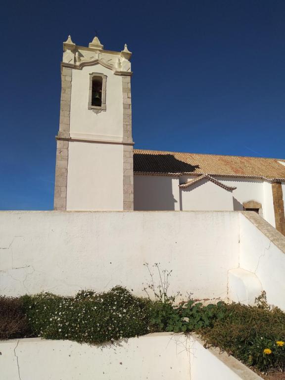 a building with a clock tower behind a white wall at Home Village in Vila do Bispo