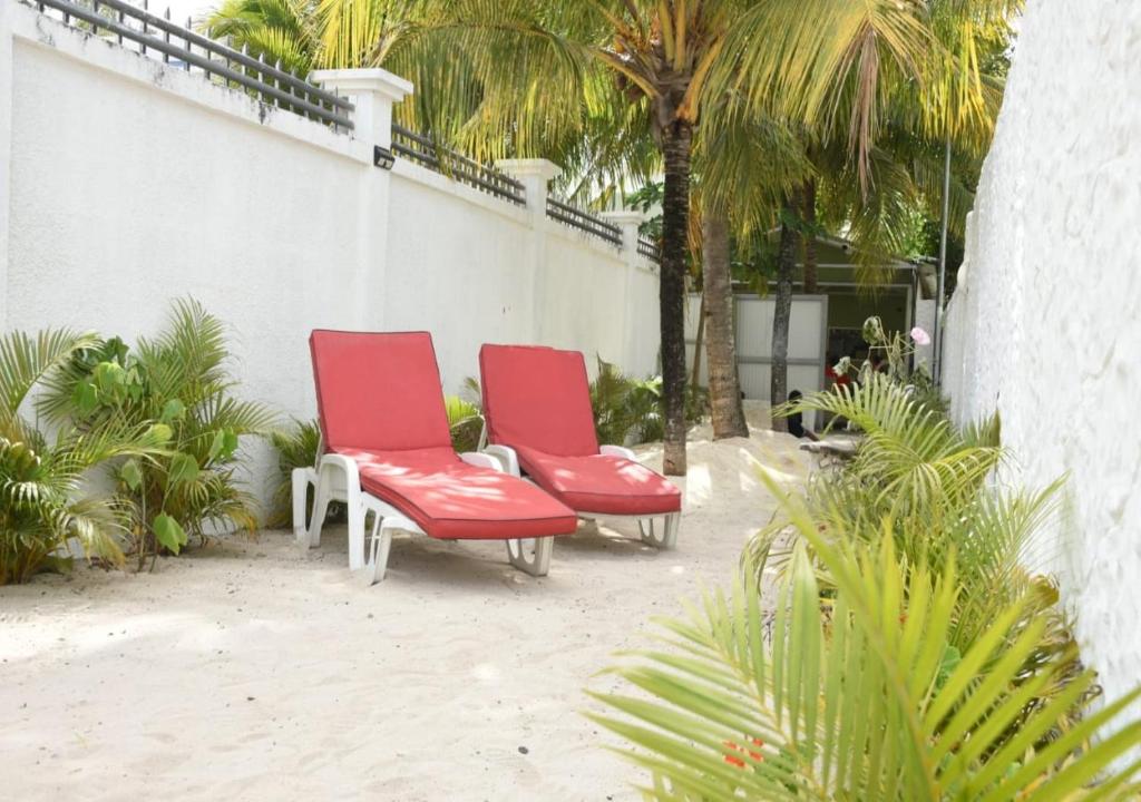 two red chairs sitting next to each other in front of a palm tree at Easy Stay Residence in Trou aux Biches