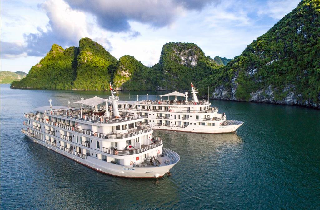 zwei Kreuzfahrtschiffe im Wasser mit Bergen im Hintergrund in der Unterkunft Paradise Elegance Cruise Halong in Hạ Long
