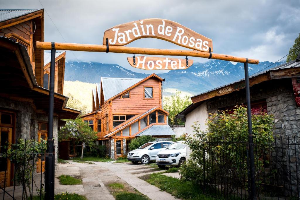 una señal para una casa de madera con coches aparcados fuera en Jardín de Rosas Hostel en El Bolsón