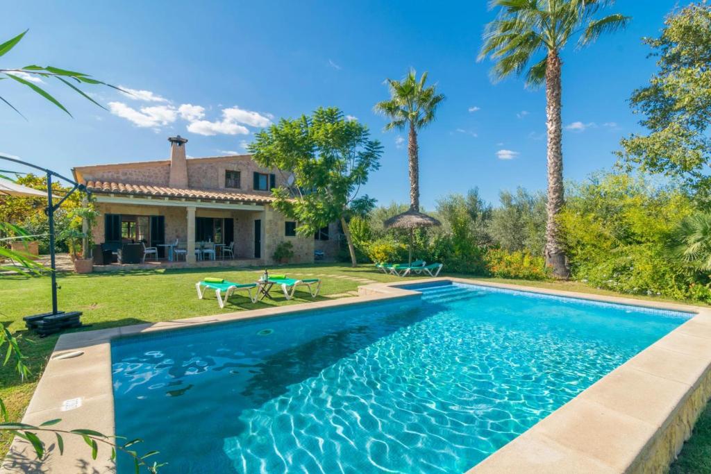 a swimming pool in front of a house with palm trees at Mercader in Alcudia
