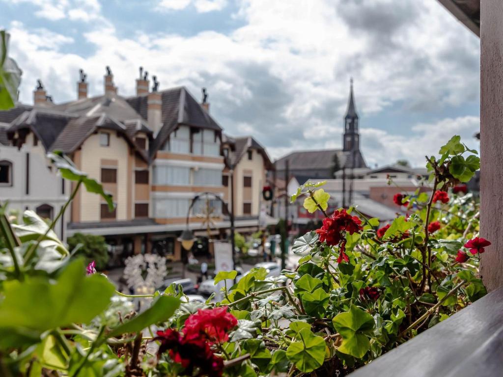 einen Balkon mit roten Blumen und Stadtblick in der Unterkunft LOCAR-IN GRAMADO- 100m Rua Coberta in Gramado