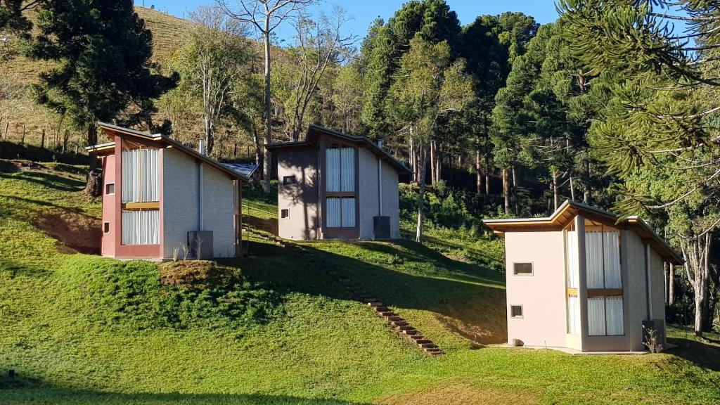 two small houses on a grassy hill with trees at Robinson Cottage Monte Verde MG in Monte Verde
