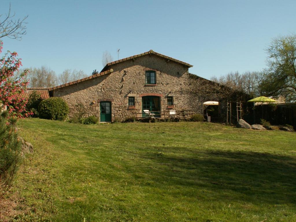 una vieja casa de piedra con un campo de hierba delante de ella en La Trainelière en Les Épesses