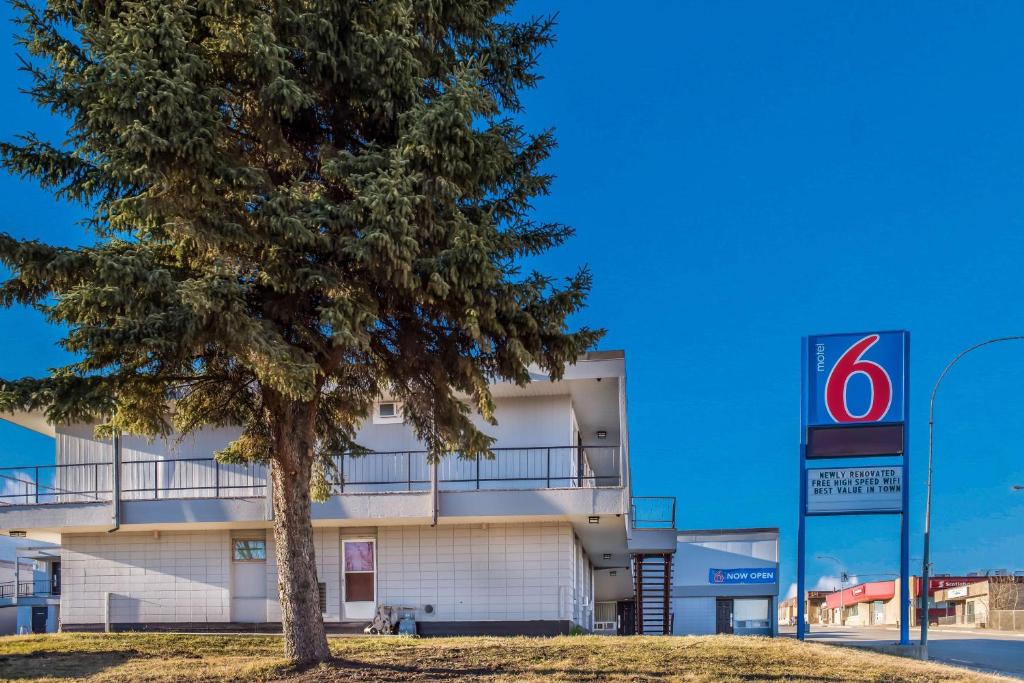 a building with a tree in front of it at Motel 6-Fort St. John, BC in Fort Saint John