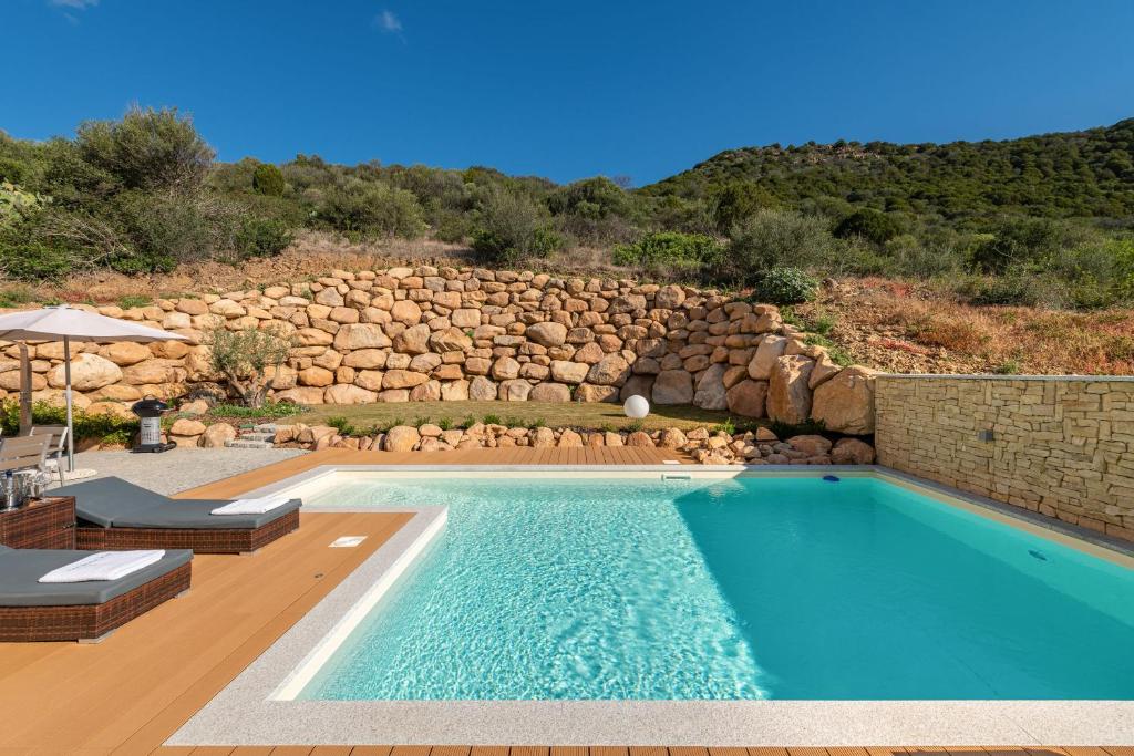 a swimming pool in a yard with a rock wall at Villa Sa Rocca Junior & Suite in Chia