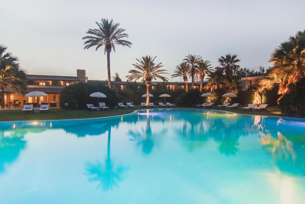a large swimming pool with palm trees and a building at Hotel Aquadulci in Chia