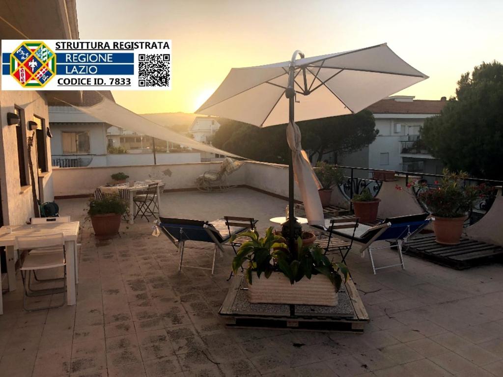 un patio con sombrilla, sillas y mesas en Attico TerraMare - 300m Beach & Maxi Terrace & BBQ, en Santa Marinella