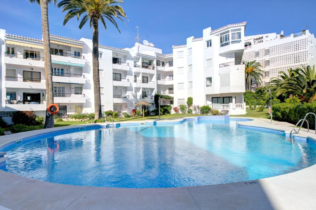 a large swimming pool with palm trees in front of buildings at Apartamento Las Palmeras in Nerja
