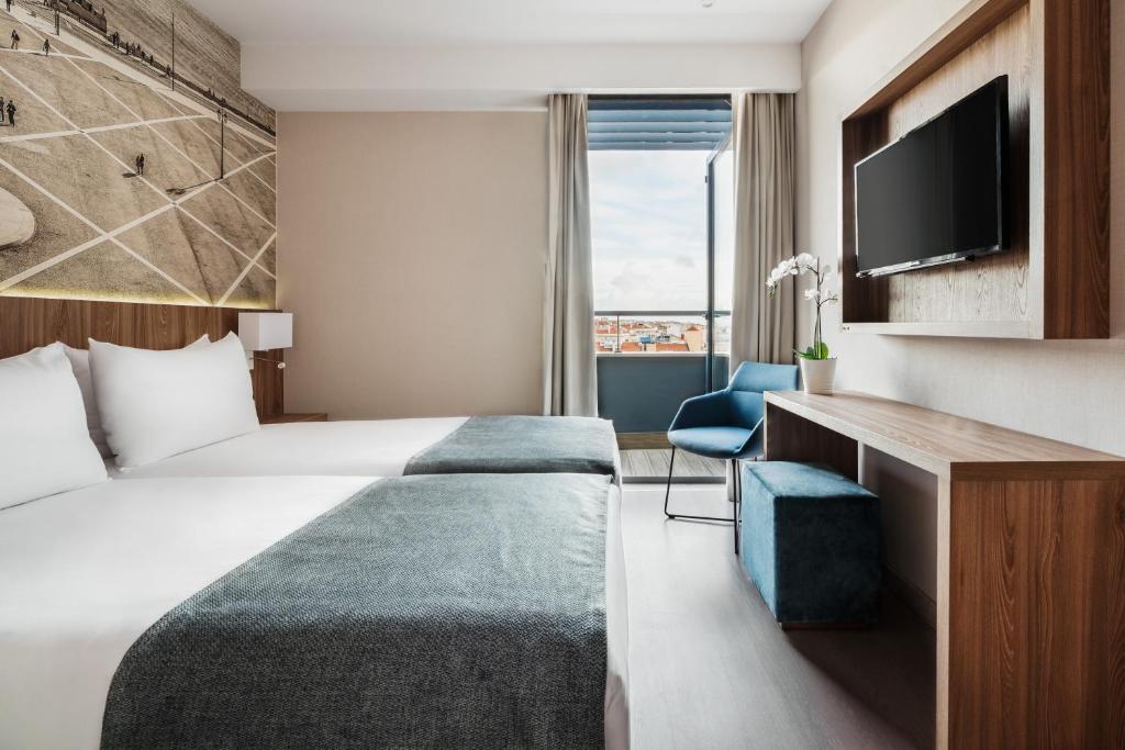 A twin room with a TV console, blue seating and a visible rooftop outlook.