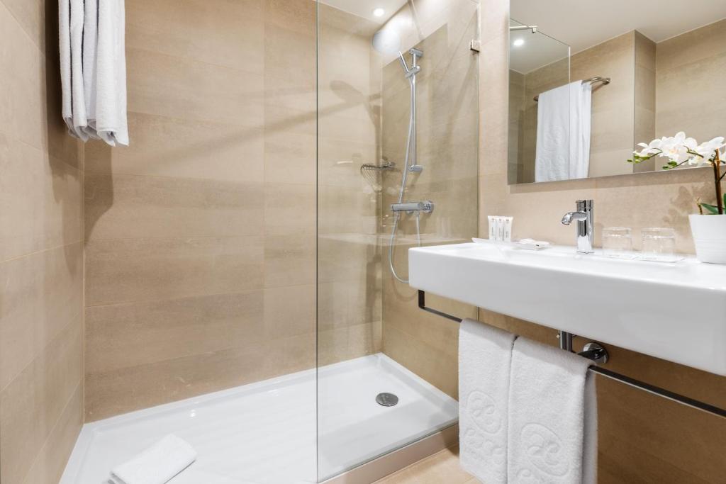A compact beige-tiled bathroom with a shower, bathtub and wall-mounted basin.